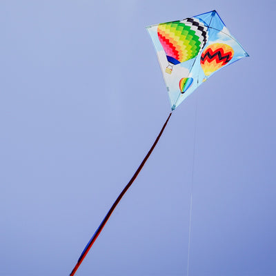 Hot Air Balloon 30" Diamond Kite with colorful design flying in a blue sky, showing vibrant colors and tails against a sunny backdrop.