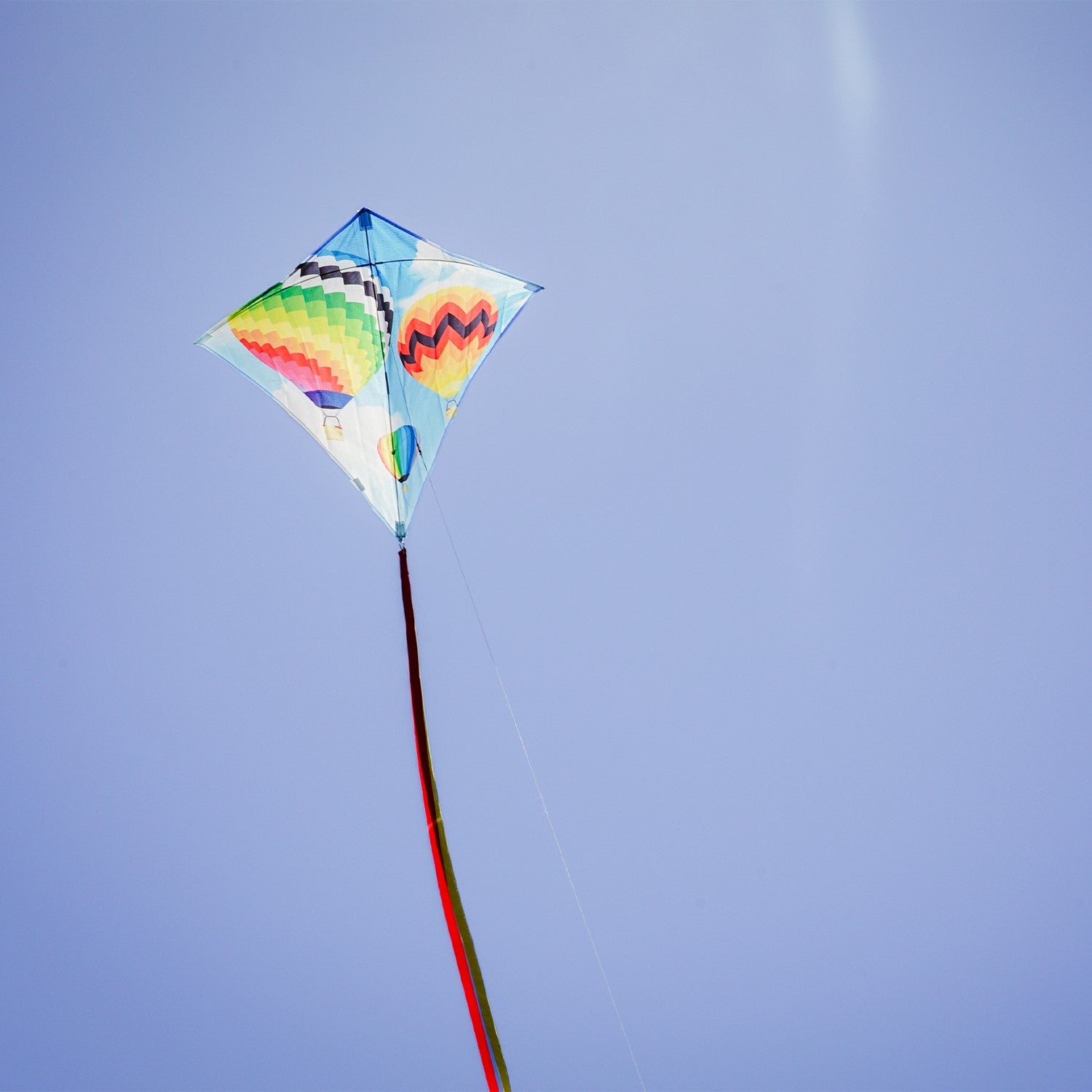 Hot Air Balloon 30" Diamond Kite with colorful design flying in a blue sky, showing vibrant colors and tails against a sunny backdrop.