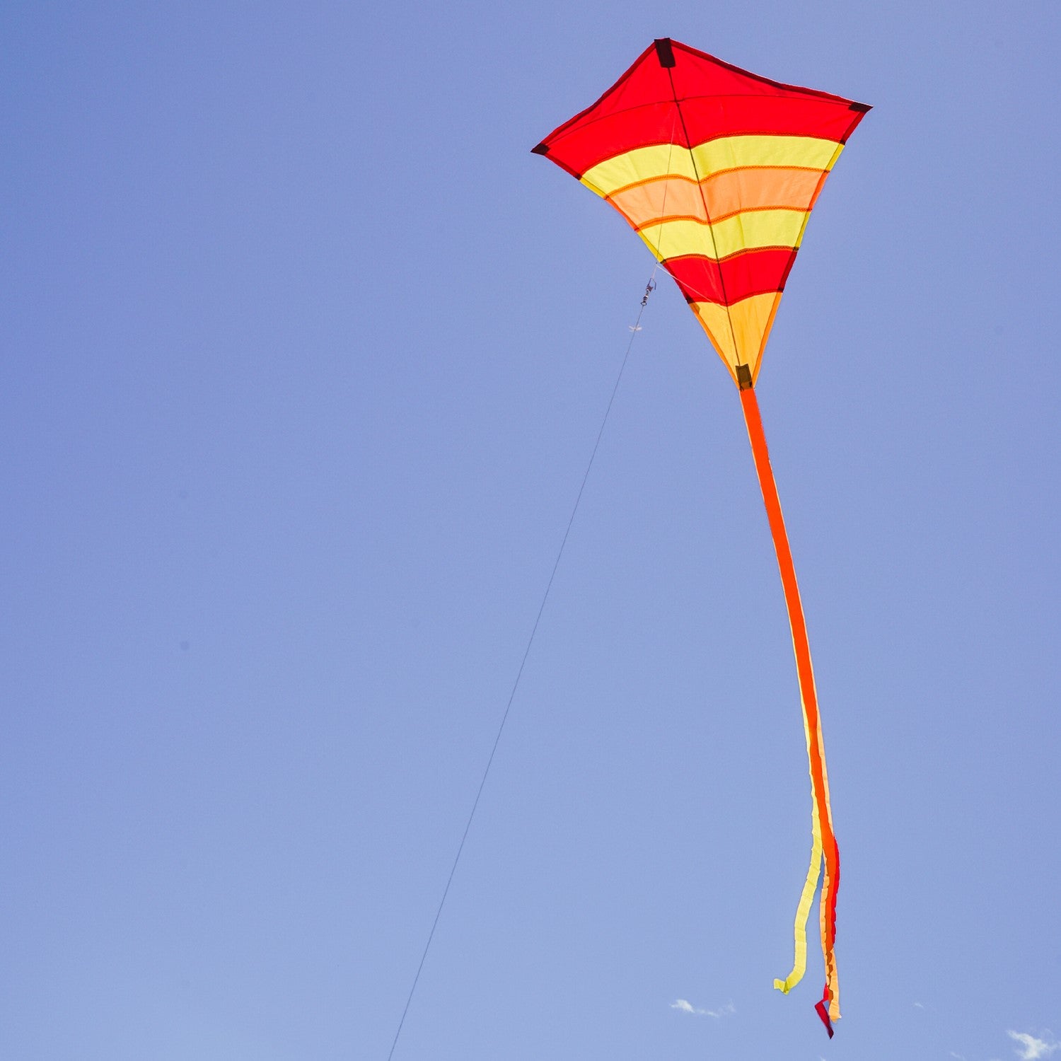 Hot Arch 27\" Diamond Kite with vibrant colors and 19-foot tails soaring in a clear blue sky, perfect for family outdoor activities.