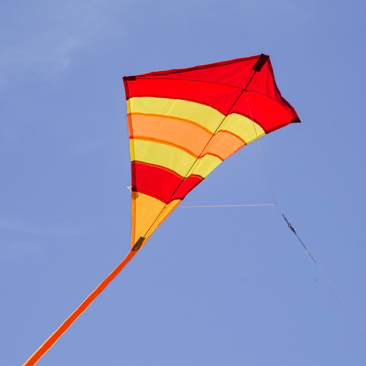 Hot Arch 27\" Diamond Kite with vibrant colors and 19-foot tails soaring in a clear blue sky, perfect for family outdoor activities.