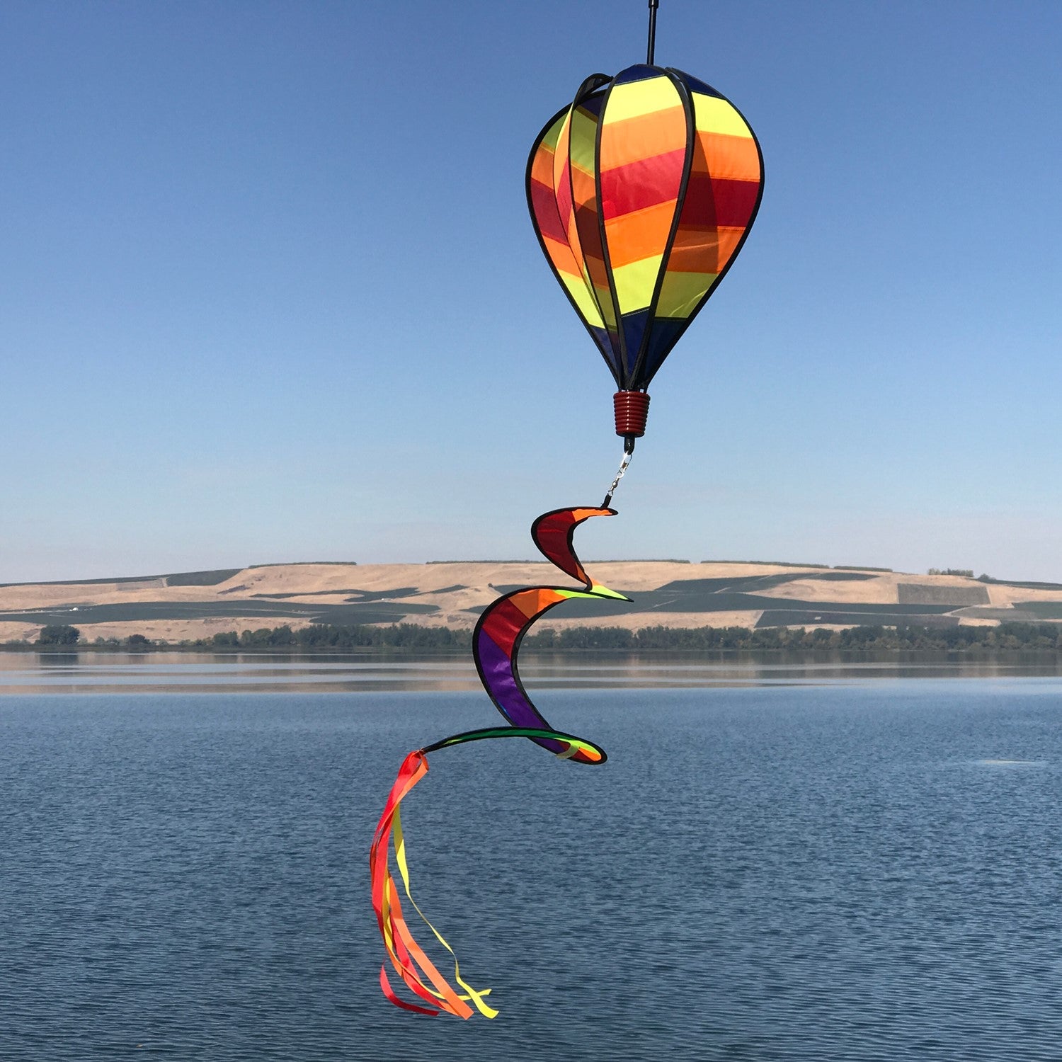 Hot Stripe Hot Air Balloon spinner with bright striped design in motion, hanging in a garden setting against a blue sky.