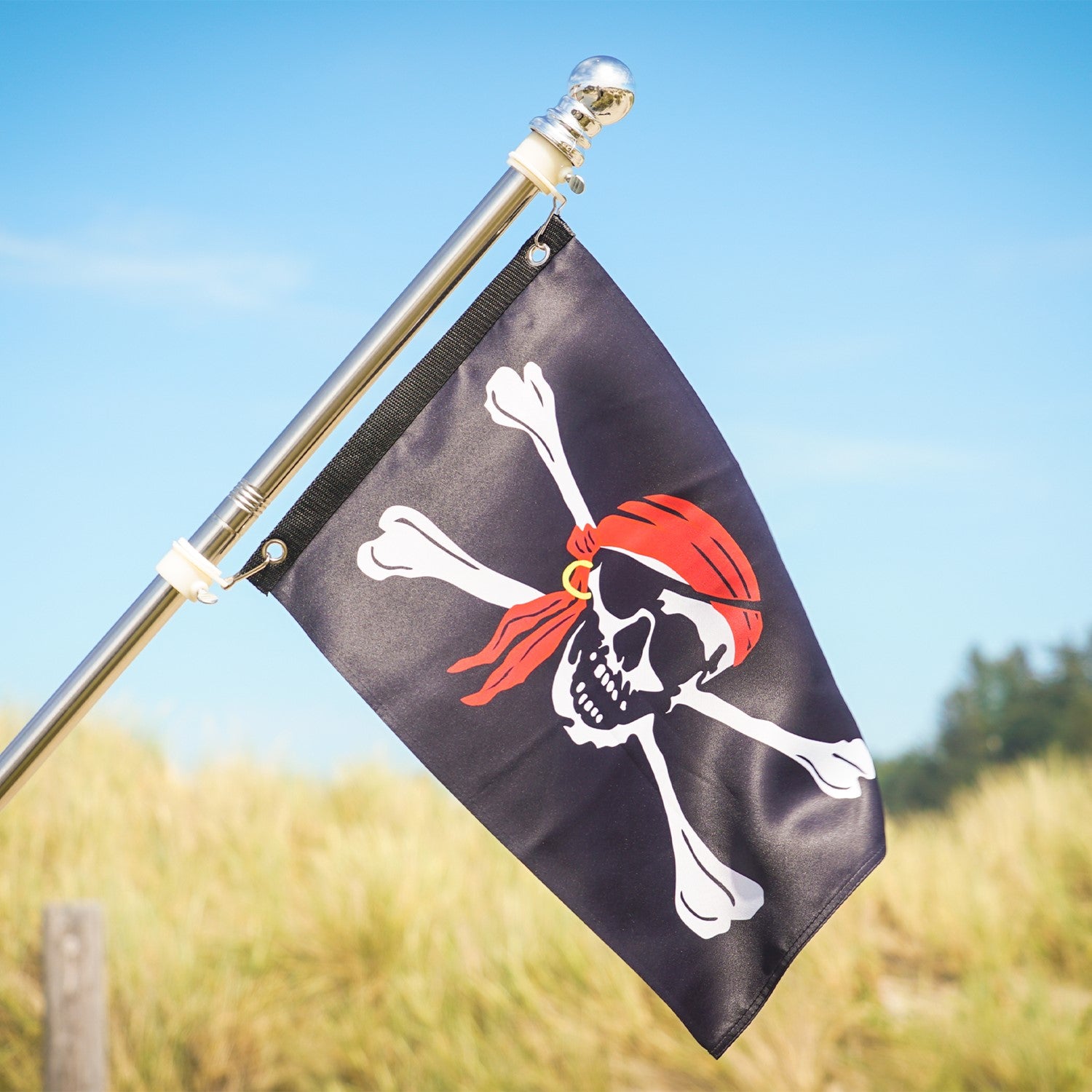 I'm a Jolly Roger Lustre 12x18 Grommet Flag featuring skull and crossbones design, displayed on a flagpole in a vibrant setting.