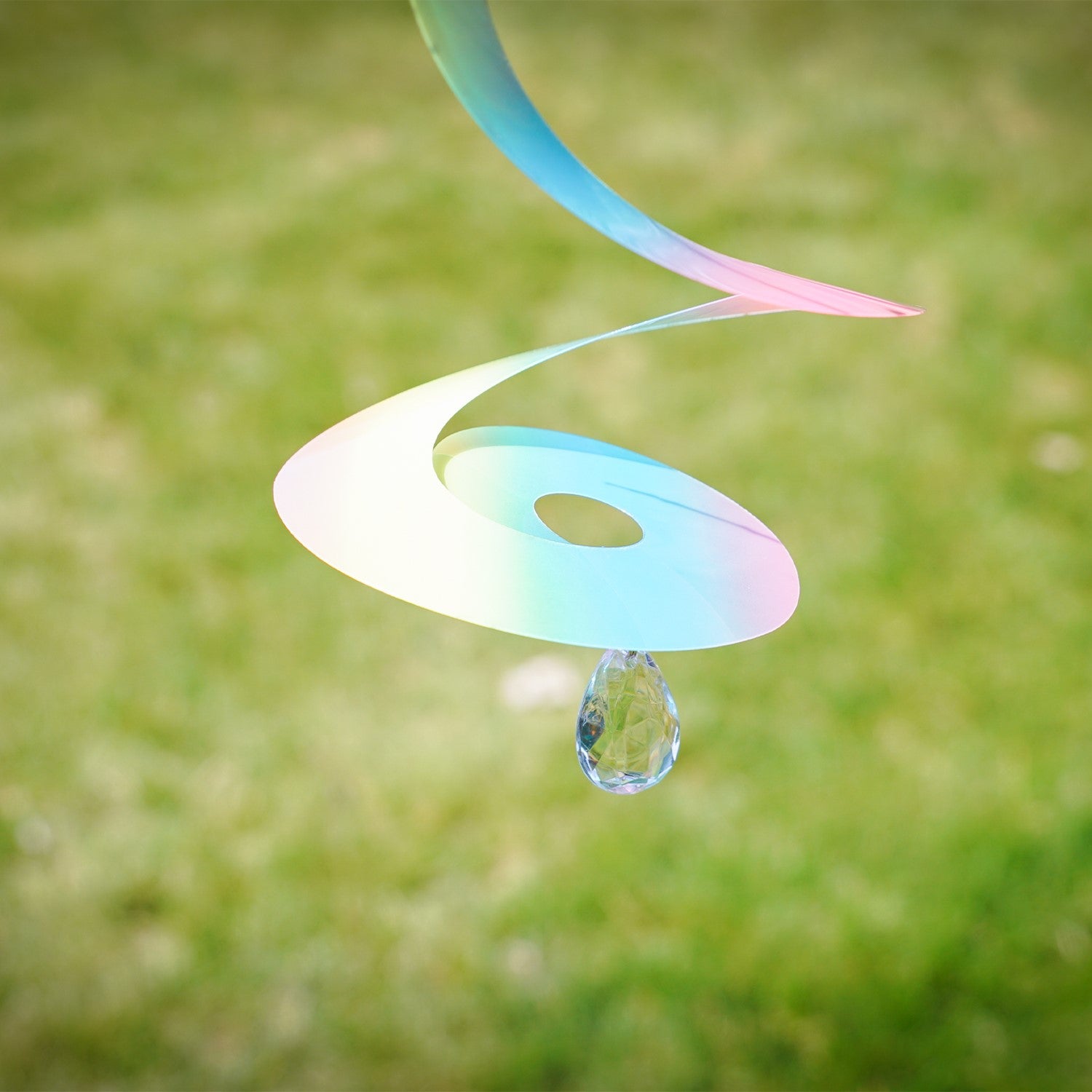 Alt Text: 8" Striped Iridescent Tear Drop Curlie with attached crystal spinner, displaying vibrant colors while hanging outdoors in a sunshine-filled garden.