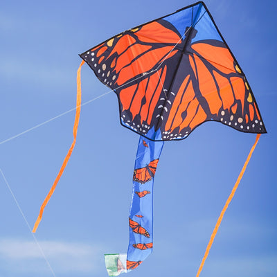 Alt text: "Monarch Swarm 45-inch Fly-Hi Kite soaring through a clear blue sky with colorful butterfly design and streamer tails.