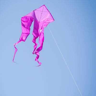 Alt Text: Purple 52" Wave Delta Kite soaring high in the sky, showcasing flowing tails and a vibrant color against a clear background.