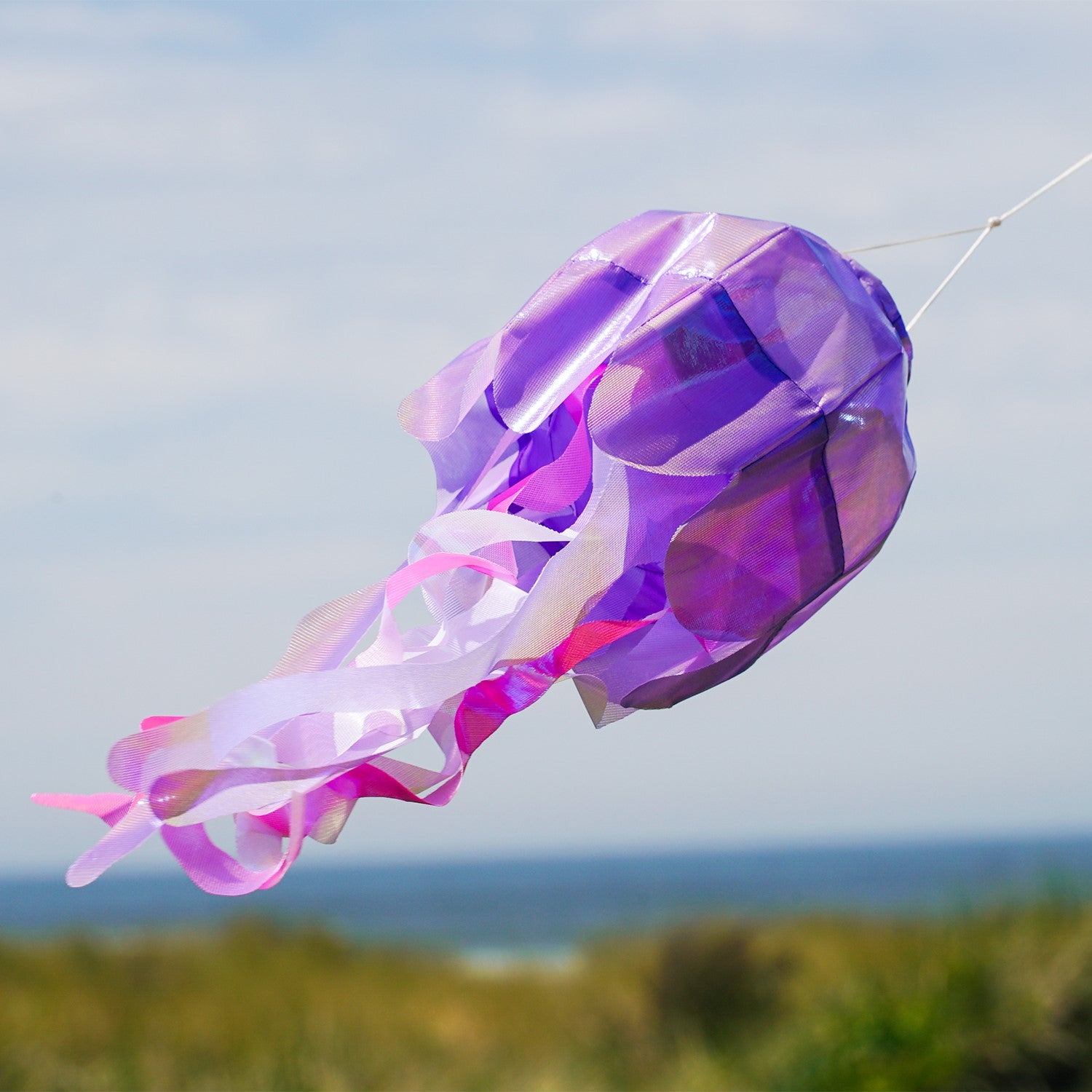 Alt text: Beautiful 15-inch Purple Iridescent Jellyfish 3D Windsock hanging outdoors, showcasing its shimmering design and flowing tentacles in the wind.