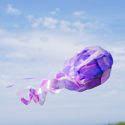 Alt text: Beautiful 15-inch Purple Iridescent Jellyfish 3D Windsock hanging outdoors, showcasing its shimmering design and flowing tentacles in the wind.