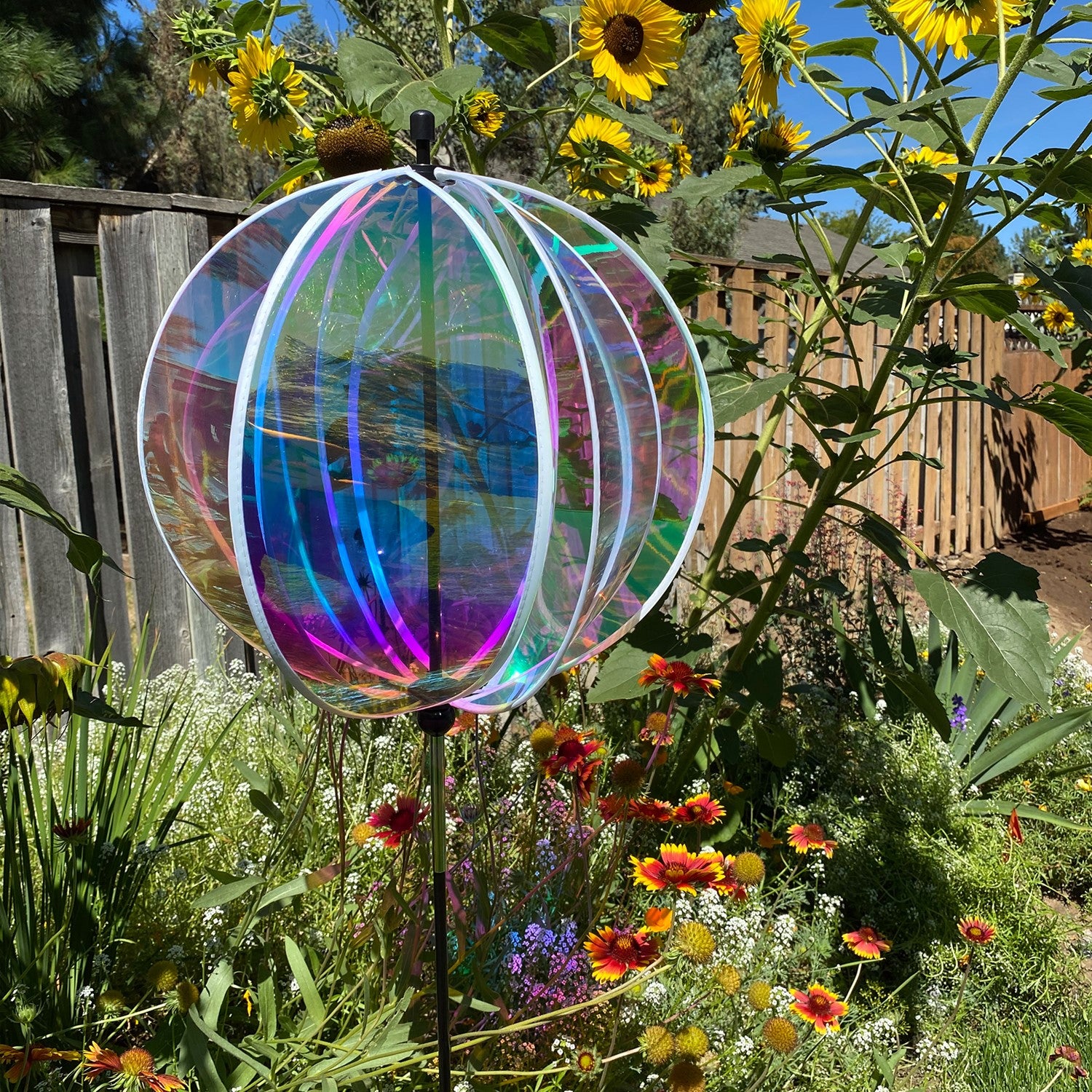 Iridescent 16-inch gazing ball spinner with six shimmering panels reflecting sunlight displayed in a vibrant garden setting.