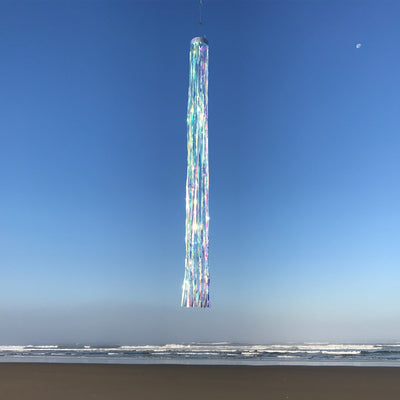 Iridescent 51-inch Mylar windsock with holographic design fluttering in a gentle breeze, creating a colorful display in a garden setting.