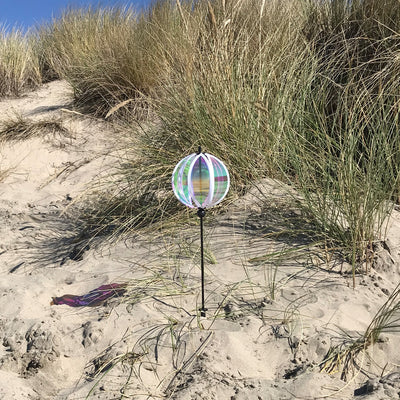 Iridescent 6-inch Gazing Ball Spinner with opalescent finish, reflecting sunlight in an outdoor garden setting, mounted on a sturdy fiberglass pole.