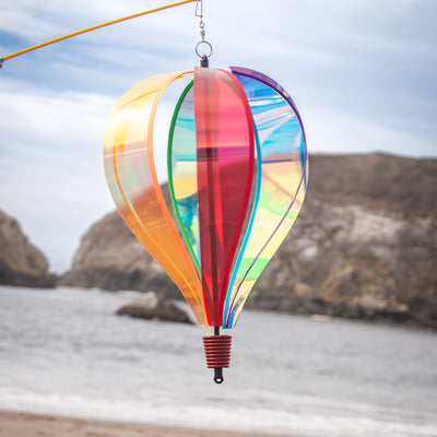 Iridescent Rainbow 6-Panel Hot Air Balloon spinner in vibrant colors, gently rotating in an outdoor garden setting.