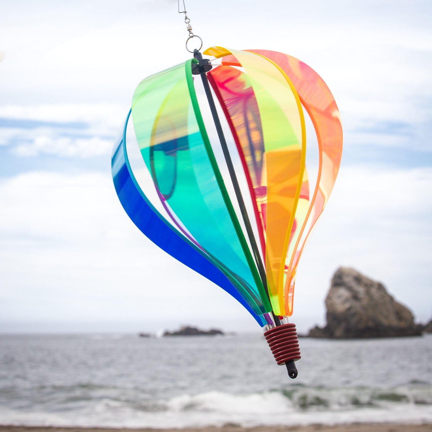 Iridescent Rainbow 6-Panel Hot Air Balloon spinner in vibrant colors, gently rotating in an outdoor garden setting.