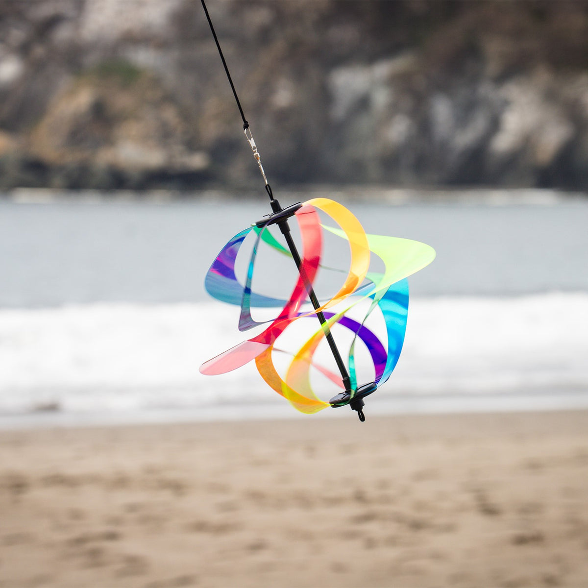 Iridescent Rainbow Vortex Spinner featuring six Mylar spirals hanging in a garden, shimmering in the breeze and reflecting light.