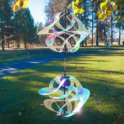 Iridescent Vortex Double Spinner showcasing interconnected Mylar spirals spinning in a sunny garden setting, creating a vibrant visual display.