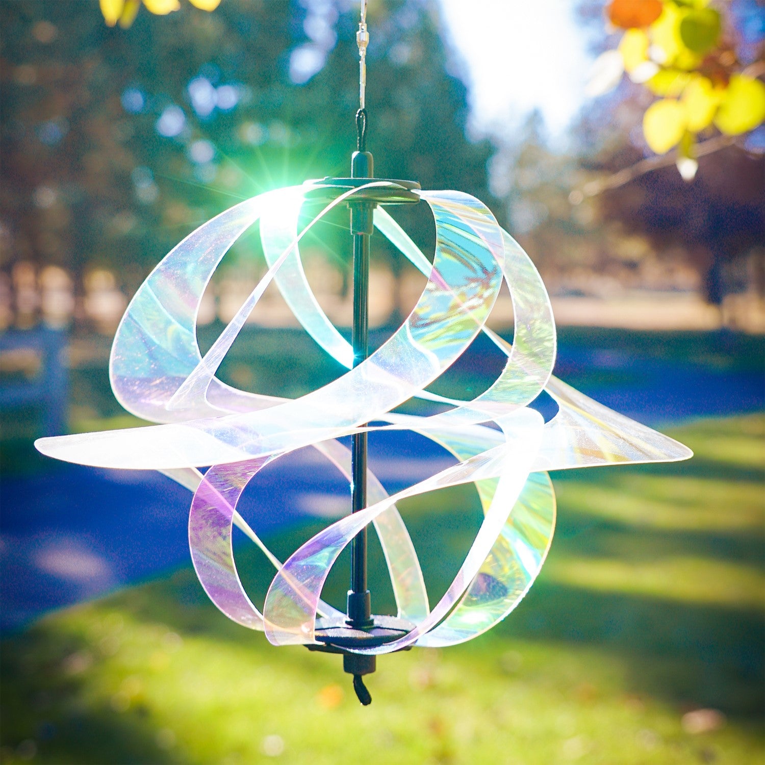 Iridescent Vortex Spinner with Mylar spirals suspended outdoors, reflecting sunlight in vibrant colors within a garden setting.