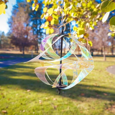 Iridescent Vortex Spinner with Mylar spirals suspended outdoors, reflecting sunlight in vibrant colors within a garden setting.