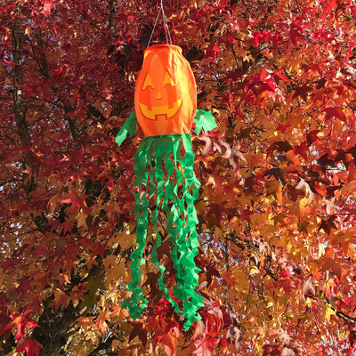 Jack O' Lantern 3D windsock featuring a vibrant pumpkin design and curlie streamer tails, displayed outdoors, fluttering in the breeze.