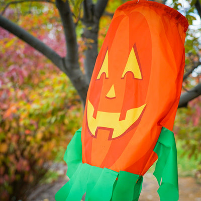 Jack O' Lantern 3D windsock featuring a vibrant pumpkin design and curlie streamer tails, displayed outdoors, fluttering in the breeze.