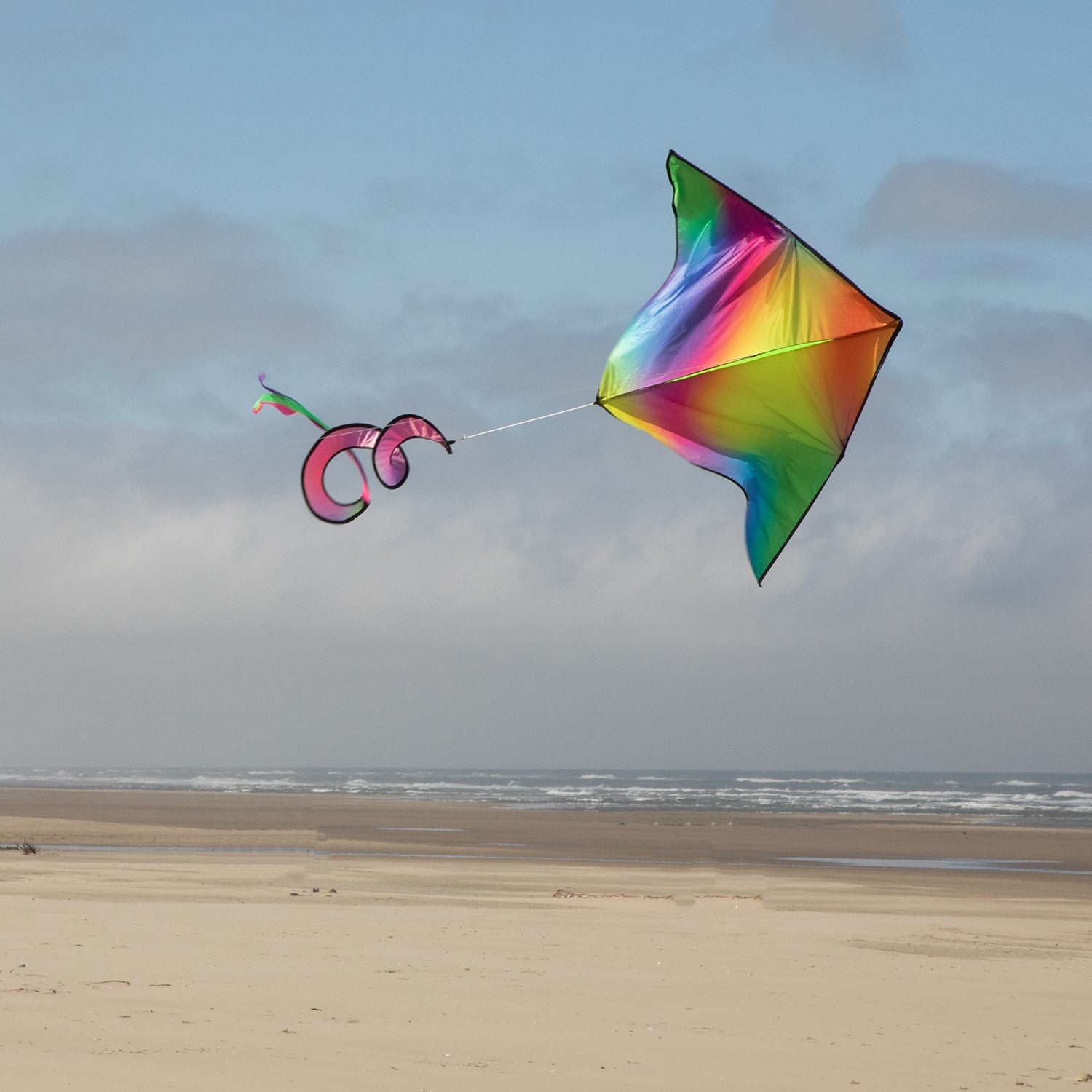 Jewel Delta with Spinning Tail kite featuring vibrant tie dye design in the sky during a sunny day, showcasing a fun outdoor activity.
