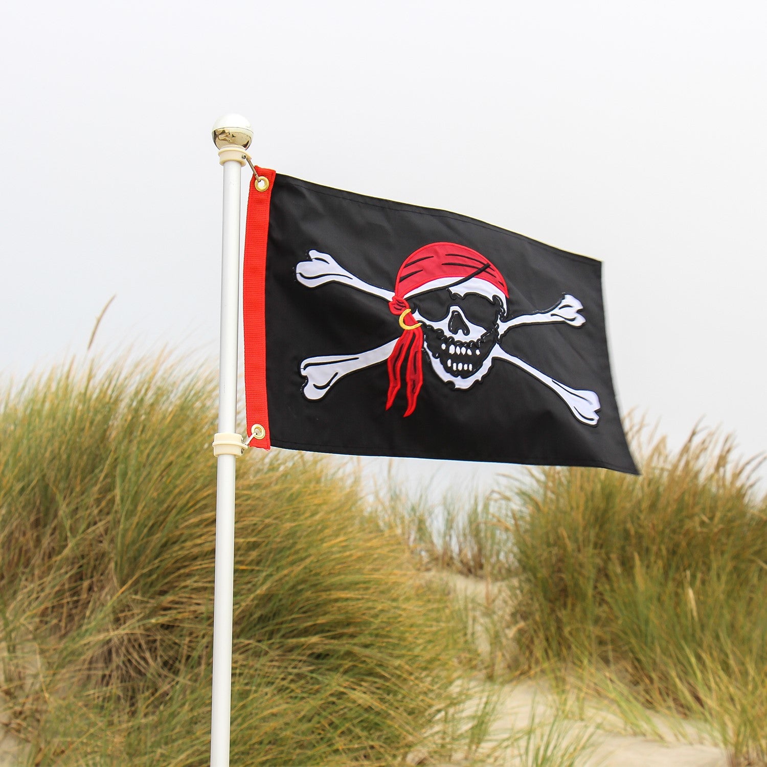 Jolly Roger Applique 12x18 Grommet Flag featuring a bold skull and crossbones design, displayed outdoors on a flagpole against a clear sky.