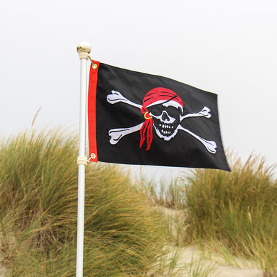 Jolly Roger Applique 12x18 Grommet Flag featuring a bold skull and crossbones design, displayed outdoors on a flagpole against a clear sky.
