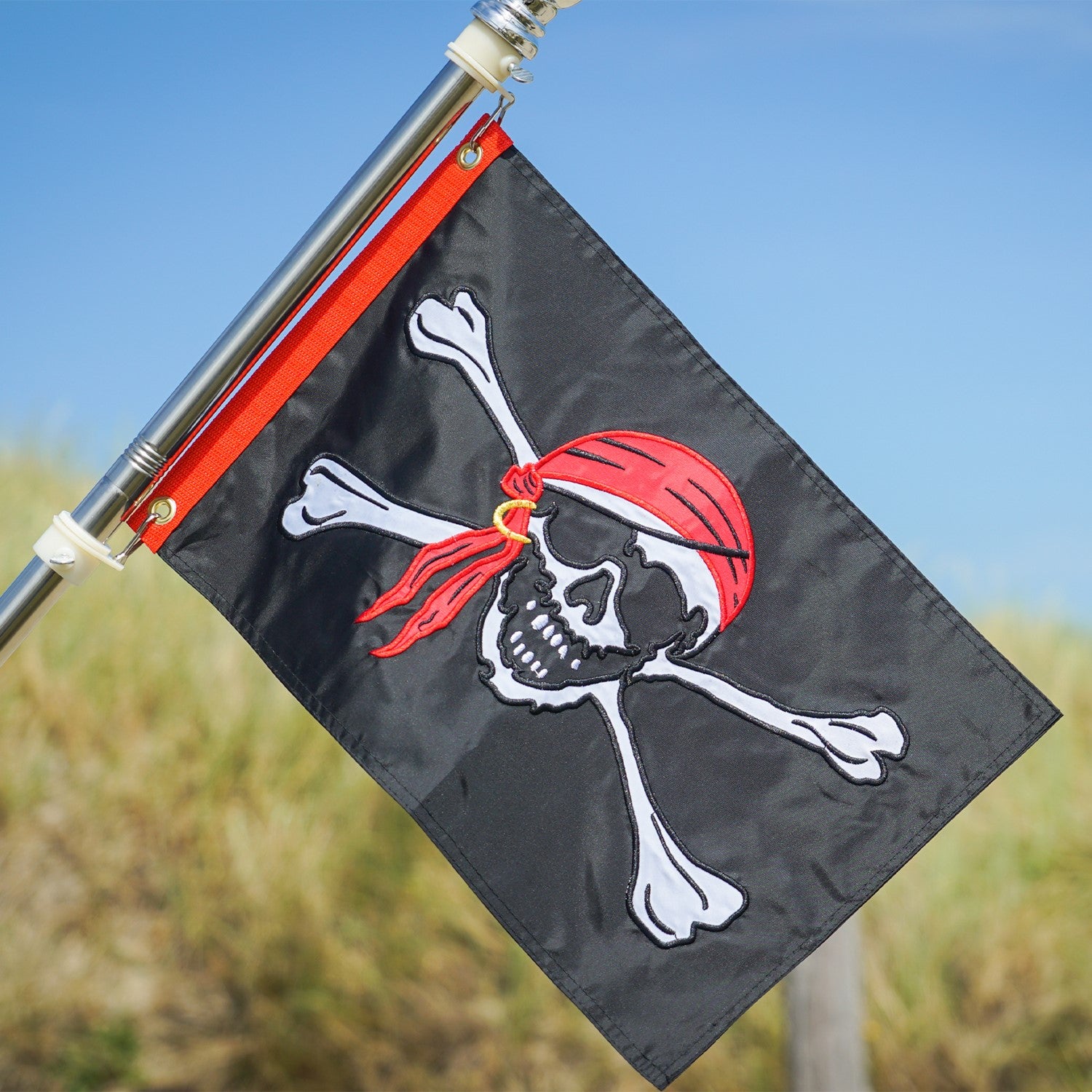 Jolly Roger Applique 12x18 Grommet Flag featuring a bold skull and crossbones design, displayed outdoors on a flagpole against a clear sky.