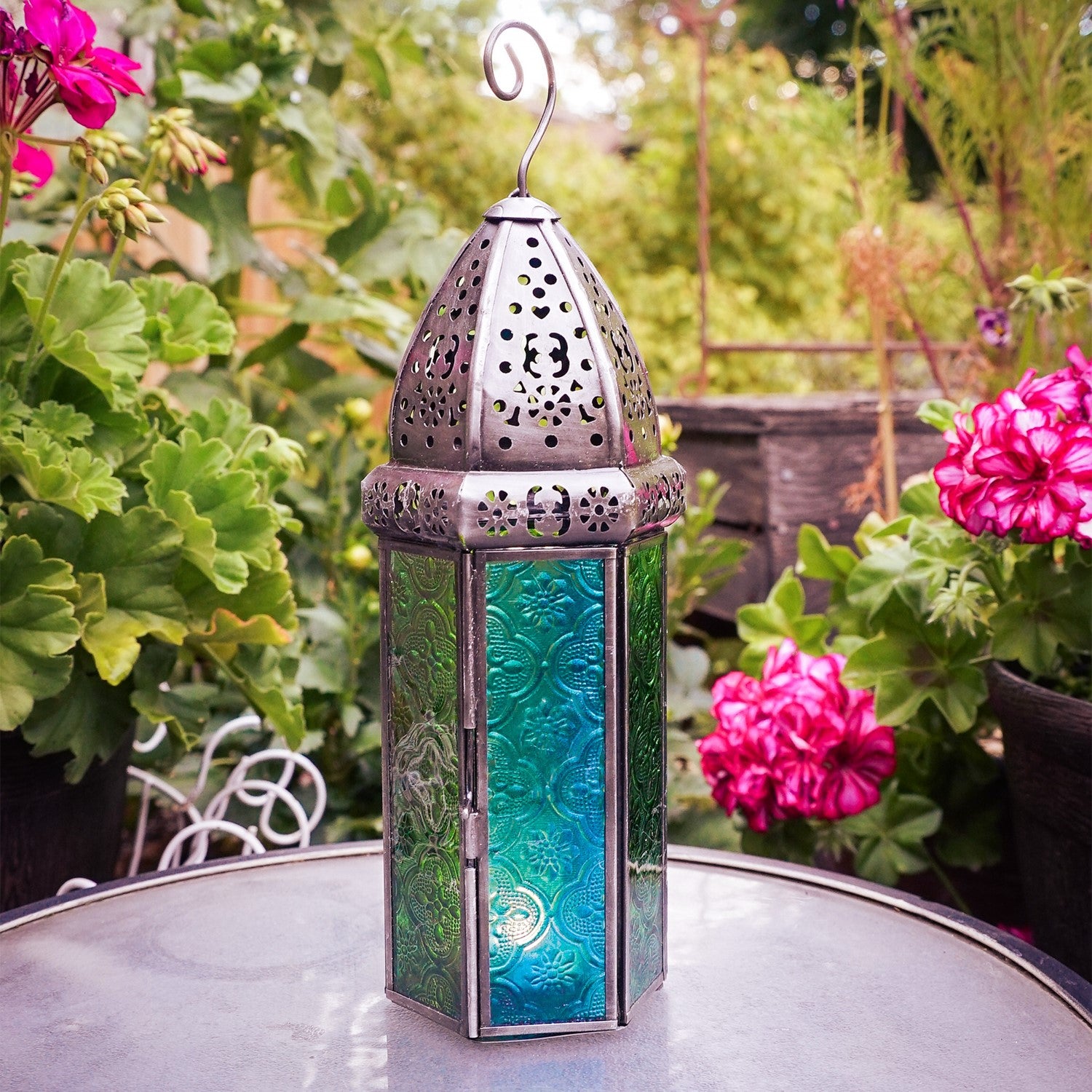 Large teal and green hex glass tealight lantern with beautiful stamped glass panels and metal frame, hanging in an outdoor setting.