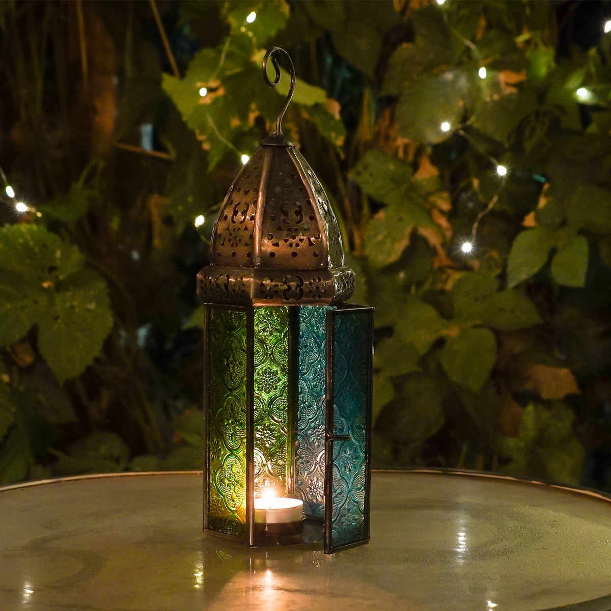 Large teal and green hex glass tealight lantern with beautiful stamped glass panels and metal frame, hanging in an outdoor setting.
