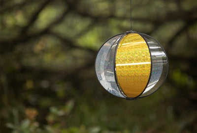 Laser Gold Spinning Globe features six glittering poly panels, designed to spin gently in the wind, displayed in a vibrant outdoor garden setting.