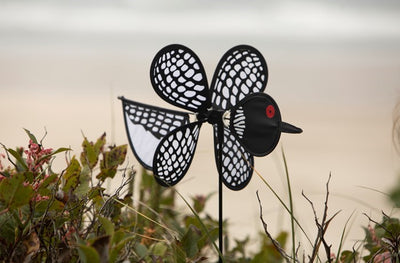 Loon Baby Spinner with colorful baby loons on a 12-inch wheel, spinning gracefully on a 17-inch fiberglass pole in an outdoor garden setting.