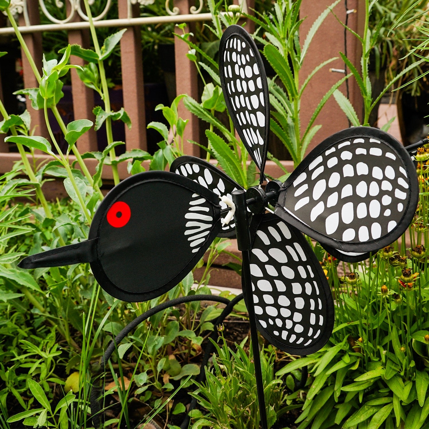 Loon Baby Spinner with colorful baby loons on a 12-inch wheel, spinning gracefully on a 17-inch fiberglass pole in an outdoor garden setting.