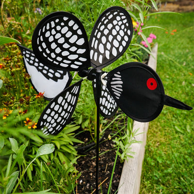 Loon Baby Spinner with colorful baby loons on a 12-inch wheel, spinning gracefully on a 17-inch fiberglass pole in an outdoor garden setting.