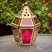 Mini Pink & Yellow Hex Glass Tealight Lantern featuring colorful stamped glass panels and a brass metal frame, displayed on a table illuminated by a candle.