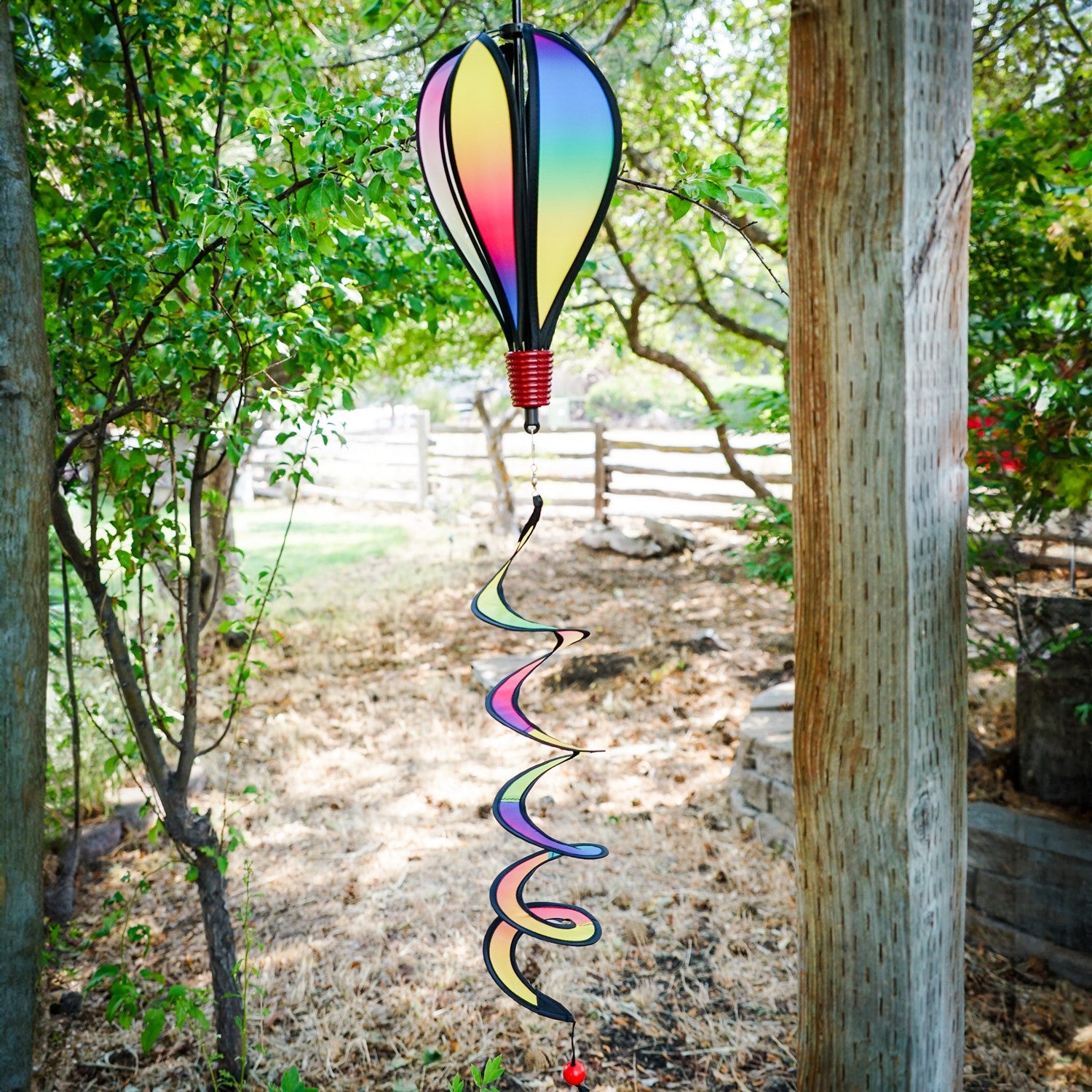 Mini Rainbow Blended Hot Air Balloon spinner with vivid colors floating gently in a garden setting, showcasing its joyful design and curlie tail.