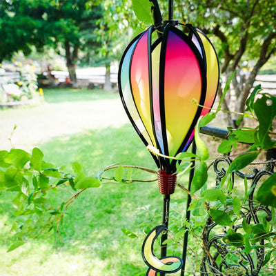Mini Rainbow Blended Hot Air Balloon spinner with vivid colors floating gently in a garden setting, showcasing its joyful design and curlie tail.