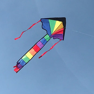 Brightly colored Mini Rainbow Fly-Hi Kite featuring a rainbow design flying in blue sky with streamer tails trailing behind it.
