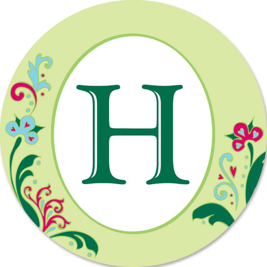 Monogram Triple Spinner - H displayed in an outdoor garden, showcasing a colorful design that spins in the wind with visible support poles.