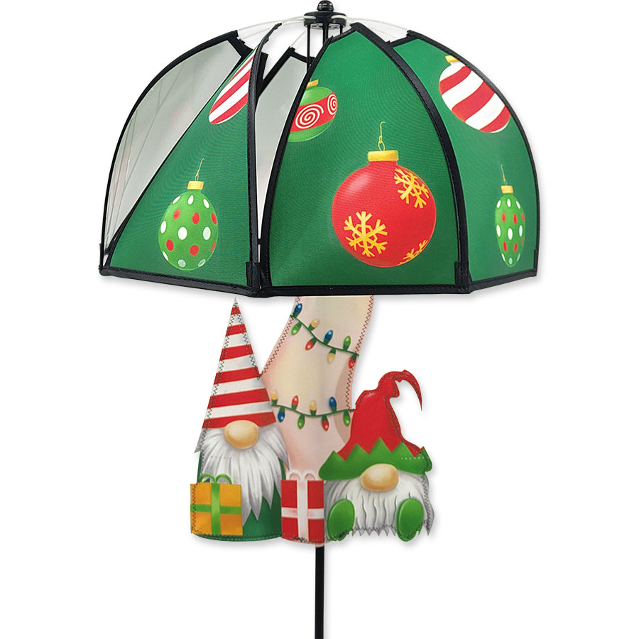 Mushroom Spinner featuring Christmas gnomes beneath a colorful umbrella, set in an outdoor garden decorated for the holidays.
