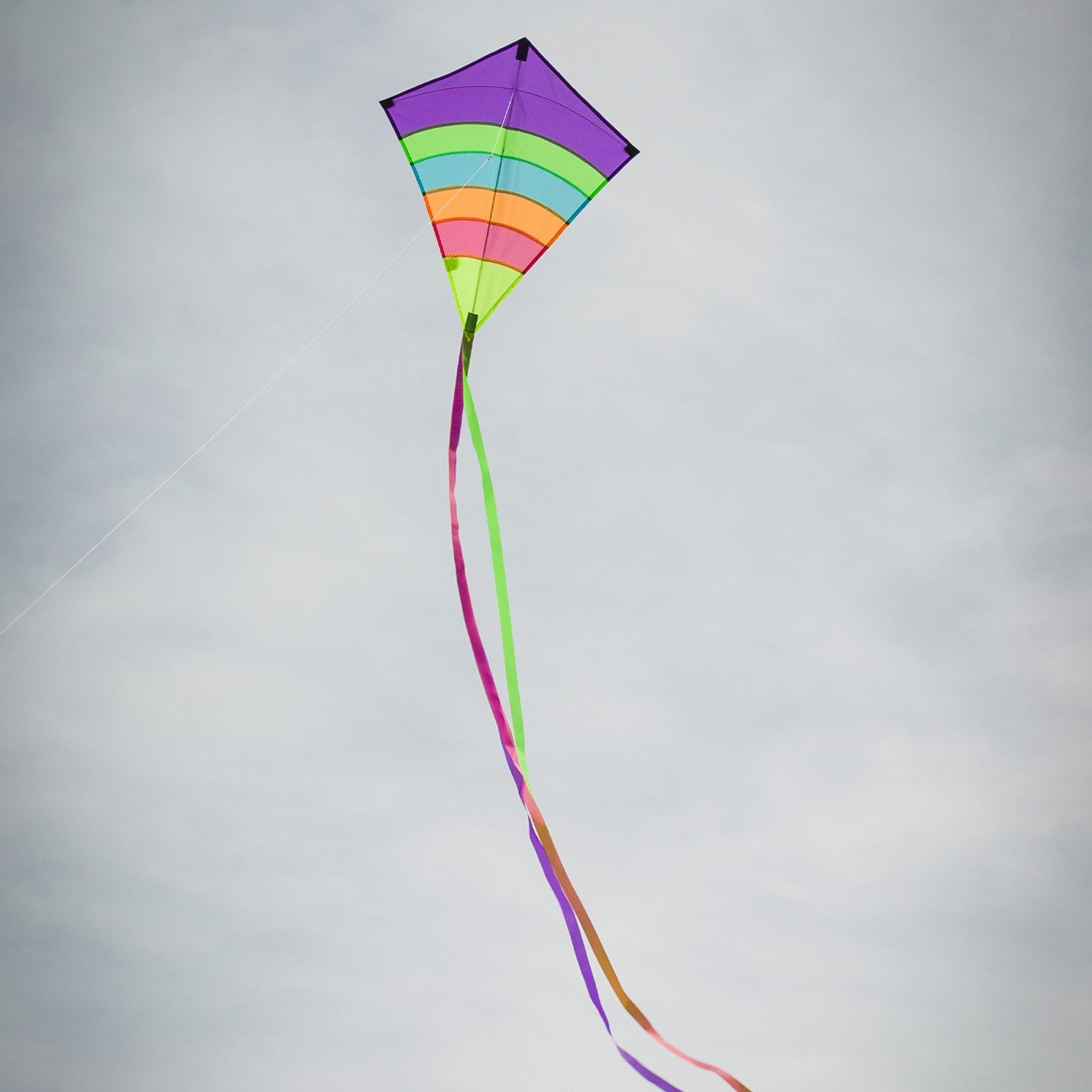 Neon Arch 27" Diamond Kite with vibrant colors and three streaming tails flying high against a blue sky in an outdoor setting.