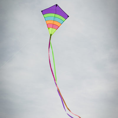 Neon Arch 27" Diamond Kite with vibrant colors and three streaming tails flying high against a blue sky in an outdoor setting.