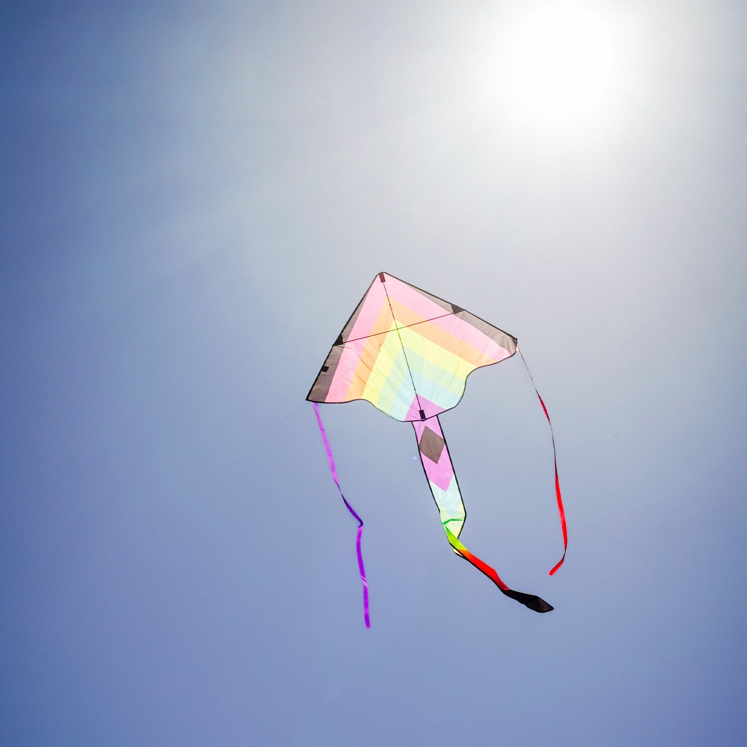 Neon Fiesta 46-inch Fly-Hi Kite soaring high in a blue sky, featuring a vibrant printed design and streamer tails, ideal for family enjoyment.