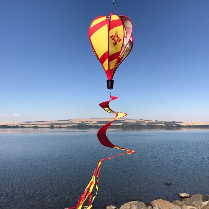 Vibrant New Mexico hot air balloon spinner with red stripes and sun design, gracefully spinning in an outdoor garden setting.