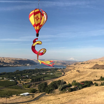 Vibrant New Mexico hot air balloon spinner with red stripes and sun design, gracefully spinning in an outdoor garden setting.