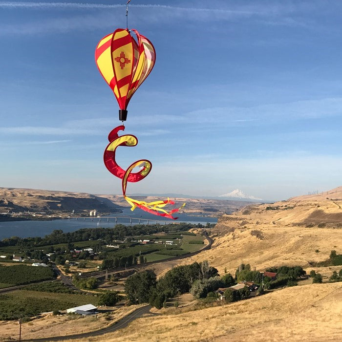 Vibrant New Mexico hot air balloon spinner with red stripes and sun design, gracefully spinning in an outdoor garden setting.