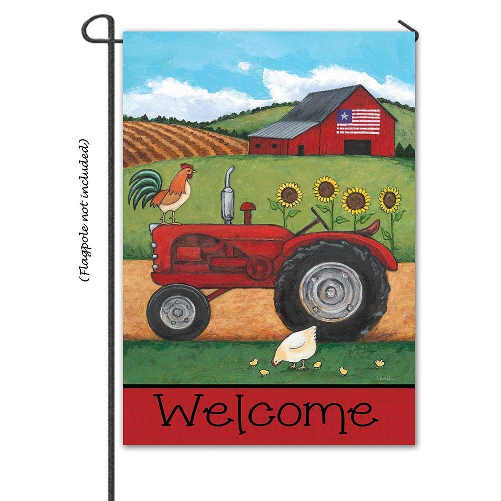 On The Farm large banner flag showcasing a farmhouse scene with vibrant colors, displayed on a flagpole in a garden setting.