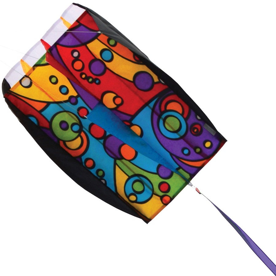 Parafoil 5 Kite - Rainbow Orbit flying high in a clear sky, showcasing its colorful design and vibrant streamers against a backdrop of greenery.