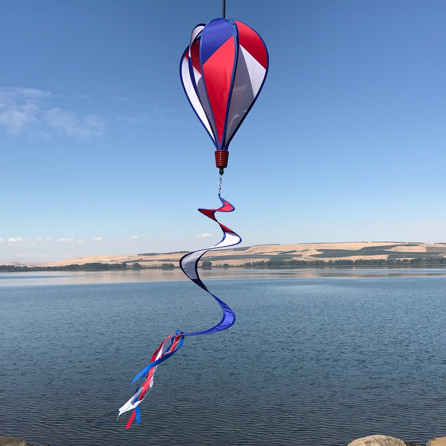 Vibrant Patriot Hot Air Balloon spinner in red, white, and blue colors gently spinning in an outdoor garden setting, showcasing its applique design.