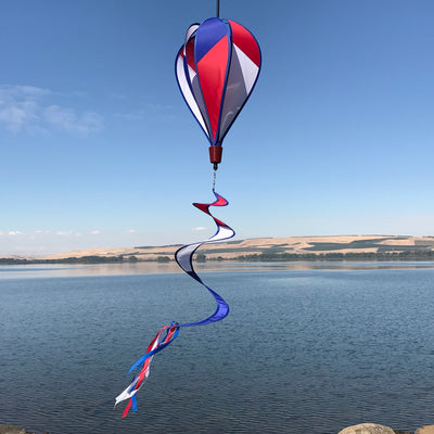 Vibrant Patriot Hot Air Balloon spinner in red, white, and blue colors gently spinning in an outdoor garden setting, showcasing its applique design.