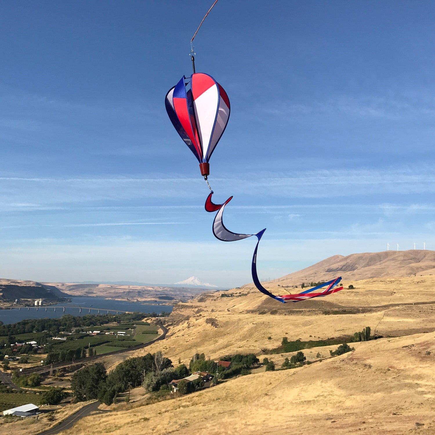 Vibrant Patriot Hot Air Balloon spinner in red, white, and blue colors gently spinning in an outdoor garden setting, showcasing its applique design.