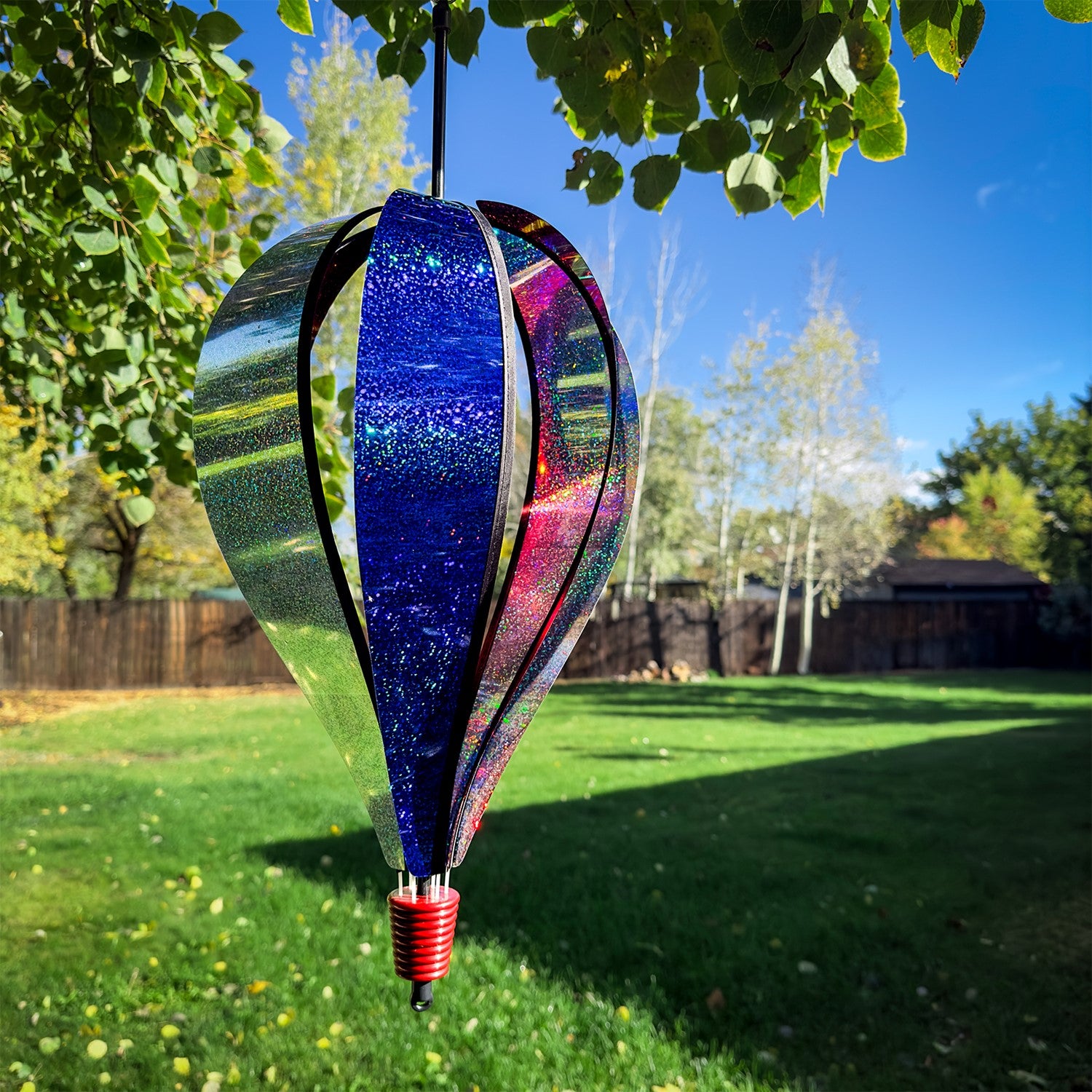 Patriot Sparkler 6-Panel Hot Air Balloon spinning in a garden, showcasing its vibrant red, white, and blue Mylar design against a blue sky.